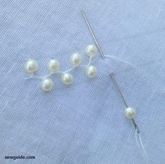 the needles are being used to make beading for beads and pearls on a piece of fabric