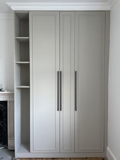 an empty room with some white cupboards and shelves on the wall next to a fireplace