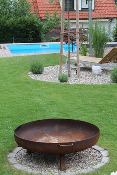 a fire pit sitting in the middle of a lush green field next to a swimming pool