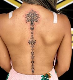 the back of a woman's neck with an intricate tattoo design on her lower back