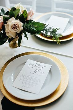 a table set with white and gold plates, napkins and flowers on top of it