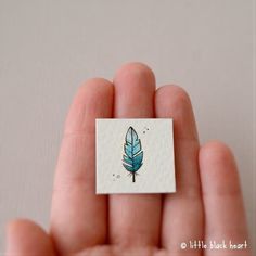 a hand holding a tiny blue feather on top of a white piece of paper in it's palm