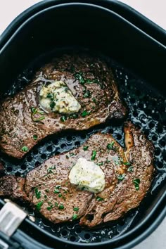 two steaks cooking in an air fryer with butter and parsley on top