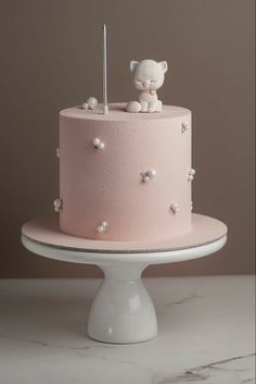 there is a pink cake with white decorations on the top, and a small cat figurine atop it