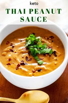 a bowl of thai peanut sauce on a wooden table with a spoon next to it