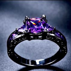 a fancy ring with an amethorate stone surrounded by black diamonds on a dark background