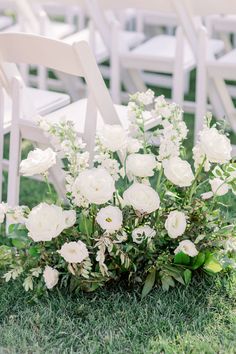 an arrangement of white flowers and greenery sits in the grass at a wedding ceremony