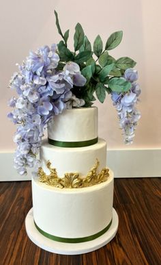 a three tiered cake with purple flowers on the top and green trimmings