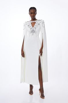 Draped In Luxury, This Dress Is Adored With Glistening Crystal Embellishments Along A Dramatic Cape Design, And Surrounding A Neck Cut Out Detail. A Midi Length Adds A Sophisticated Touch While A Split Hem Offers Allure. Pair With Barely-There Heels And Silver Accessories For Stand-Out Formal Wear.Crystal Embellishmentscut Out Detailcape Design Fitted Embellished Dress With Cape Sleeves, Embellished Cocktail Dress With Cape Sleeves, Cocktail Dress With Embellished Cape Sleeves, Embellished Cocktail Dresses With Cape Sleeves, Embellished Evening Dresses With Cape Sleeves, Evening Dresses With Pearl Embroidery And Cape Sleeves, Elegant White Dress With Pearl Embroidery, Hand Embellished Fitted Dress With Cape Sleeves, Fitted Hand Embellished Dresses With Cape Sleeves