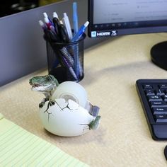 a computer monitor sitting on top of a desk next to a white egg with a lizard in it