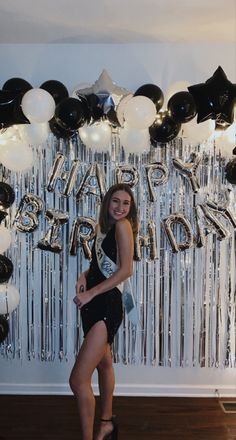 a woman standing in front of balloons and streamers with the words happy birthday on it