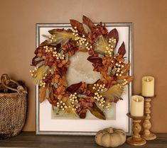 a wreath with leaves and berries is on a mantle next to a lit candle in a wicker basket