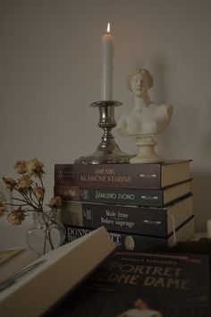 a stack of books sitting on top of a table next to a candle and vase