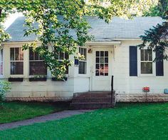 a small white house with black shutters on the front and side windows is shown