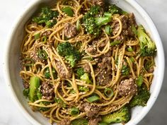 a white bowl filled with noodles, broccoli and ground beef on top of a marble table