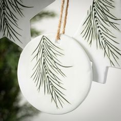 two white ornaments hanging from a string with pine needles on them, one is round and the other is circular