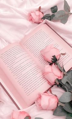 an open book sitting on top of a bed next to pink roses and eucalyptus leaves