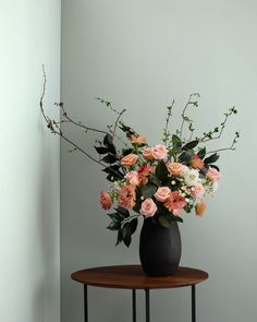 a black vase filled with pink and white flowers on top of a small wooden table