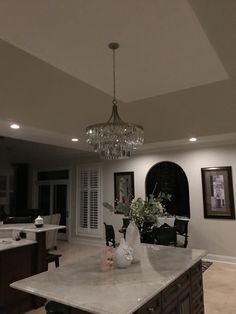 a chandelier hanging from the ceiling in a large kitchen with marble counter tops