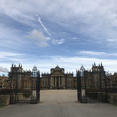 a large building with an iron gate in front of it and a sky filled with wispy clouds