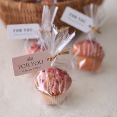 three small cupcakes wrapped in plastic wrappers on a table next to a basket