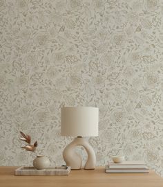 a table with a lamp and some books on it next to a wallpapered wall