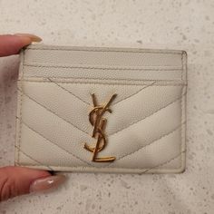 a white card holder with a gold saint laurent logo on it