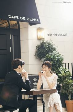 a man and woman sitting at a table in front of a building with plants on it