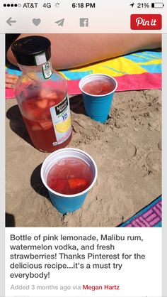 two plastic cups filled with liquid sitting on top of a beach next to a bottle