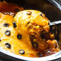 a crock pot filled with chicken and black olives being scooped from the slow cooker