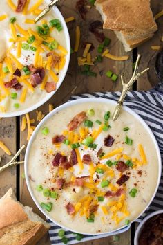 two bowls of potato soup with bacon, cheese and green onions on the table next to bread