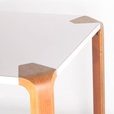 a white table with wooden legs and a glass top that has a brown wood edge