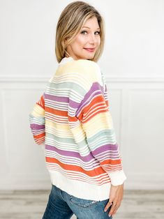 a woman standing in front of a white wall wearing a multicolored striped sweater