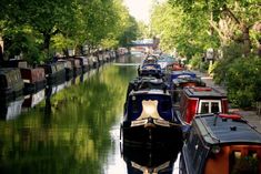 several boats are lined up along the side of a narrow canal with trees lining both sides