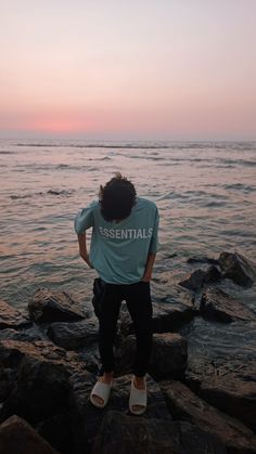 a man standing on rocks near the ocean with his back to the camera and looking at the water