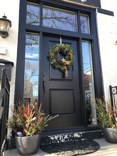 a black front door with a wreath on it and potted plants outside the door