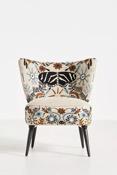 an upholstered chair with flowers and butterflies on the back, against a white background