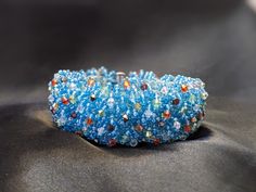 a blue bracelet with multicolored beads on top of a black cloth covered table