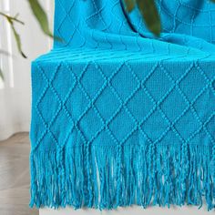 a blue blanket sitting on top of a white table next to a plant in a vase