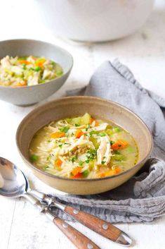 two bowls of chicken noodle soup on a white table