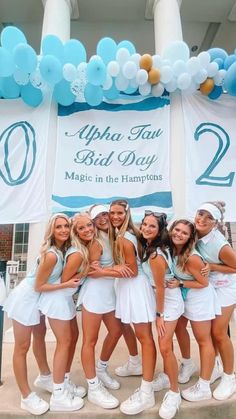 a group of young women standing next to each other in front of a sign with balloons