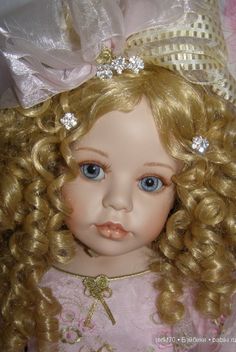 a close up of a doll with blonde hair and blue eyes wearing a tiara