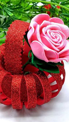 a pink rose sitting on top of a red hair clip with glitter ribbon around it