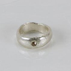 a silver ring with a brown diamond on it's center, sitting on a white surface