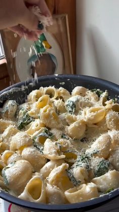 a pan filled with pasta and spinach on top of a table next to a window