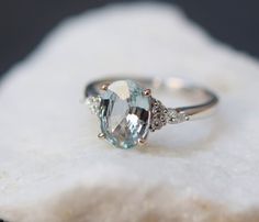 an oval cut aquamarinee and diamond ring sitting on top of a white rock