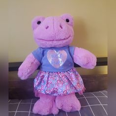 a pink stuffed animal with a heart on it's chest sitting on a tile floor