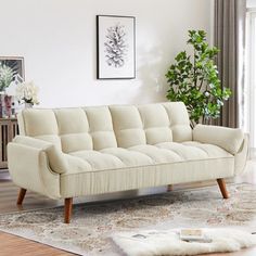 a white couch sitting on top of a wooden floor next to a plant in a living room