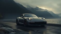 a grey sports car driving down a wet road next to the ocean with mountains in the background