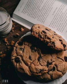 two chocolate chip cookies sitting on top of a white plate next to a glass of milk